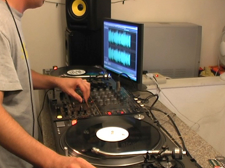 photo of two turntables, a monitor and a person adjusting a soundboard